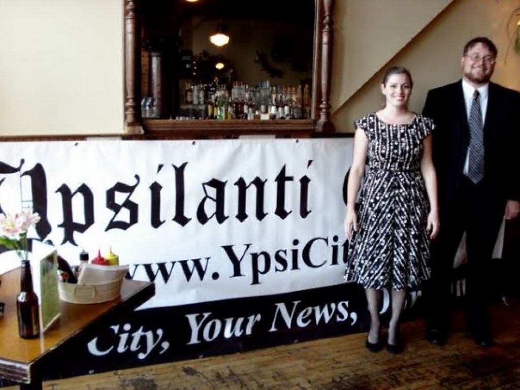Christine Laughren and Dan DuChene, co-owners of the Ypsilanti Citizen, pose in front of their company's banner at Frenchie's during the Citizen's one-year anniversary party.