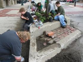 Volunteers and W.H. Canon employees plant flowers in Depot Town while Ypsilanti resident Mike Labadie repairs the planter's brick work on Ypsi PRIDE Day last year.